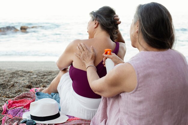 해변에서 뒷면에 자외선 차단제를 적용하는 노인 여성