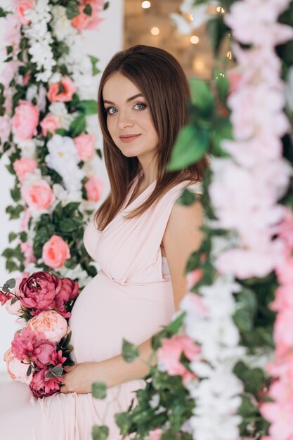 임신 한 여자의 민감한 초상화입니다. 핑크 드레스에 기대 여자 꽃 포즈