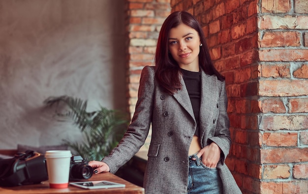 Sensual brunette woman dressed in trendy clothes posing in a room with loft interior, looking at camera.