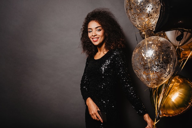 Sensual curly woman posing on wall with party balloons