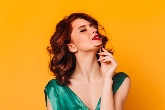 Sensual curly woman posing with closed eyes Studio shot of relaxed ginger girl isolated on yellow background