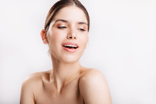 Sensual dark blond lady without make-up poses for portrait without filters on white wall.