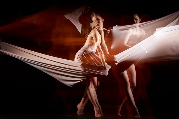 The sensual and emotional dance of beautiful ballerina with white fabric