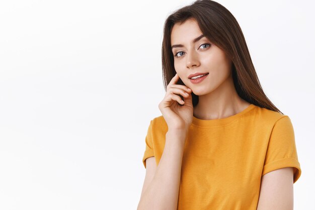 Sensual feminine brunette female in yellow tshirt open mouth flirty touching cheek and gazing camera dreamy or pensive smiling coquettish feeling selfacceptance pleased with own body