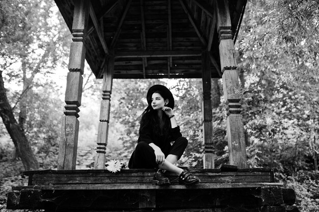 黒と赤の唇と帽子の官能的な女の子森の木製のアーチに座っているゴス劇的な女性黒と白の肖像画