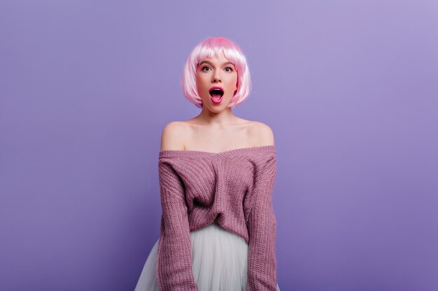 놀랍게도 찾고 짧은 분홍색 머리를 가진 관능적 인 소녀. 보라색 벽에 고립 된 흰색 치마에 웅장 한 젊은 아가씨의 실내 사진.