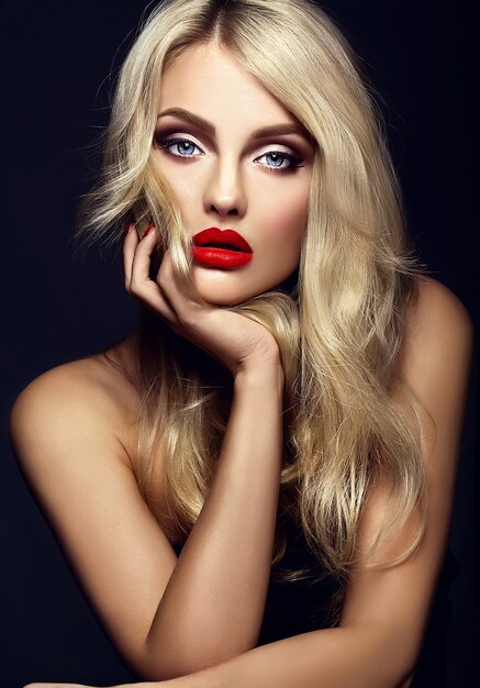 明るいメイクと赤い唇、黒い背景に健康的な巻き毛の美しい金髪の女性モデルの女性の官能的な魅力の肖像画