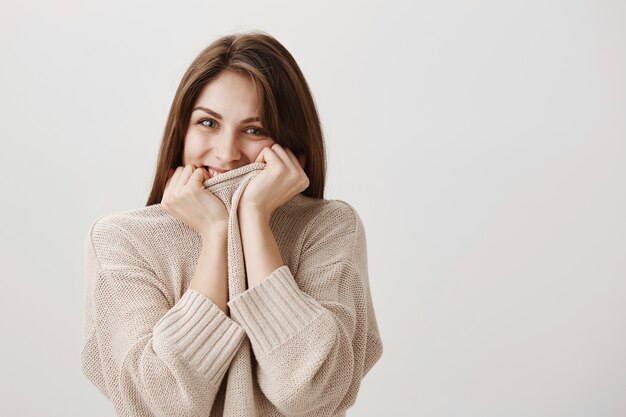 官能的な幸せな女性は笑い、セーターの後ろに笑顔を隠す