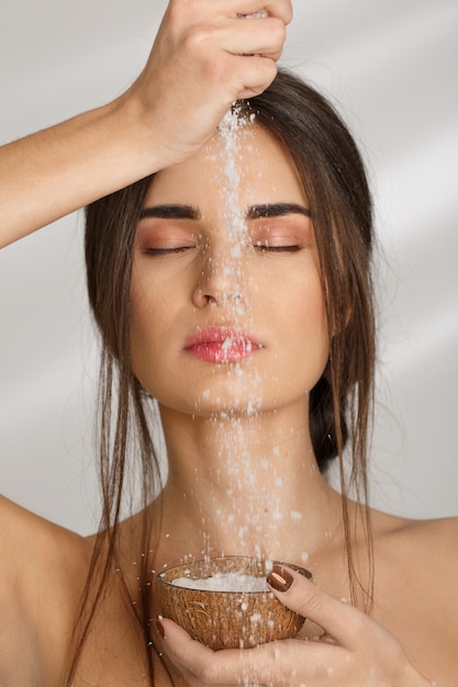 Sensual lady with eyes closed pouring salt body scrub.