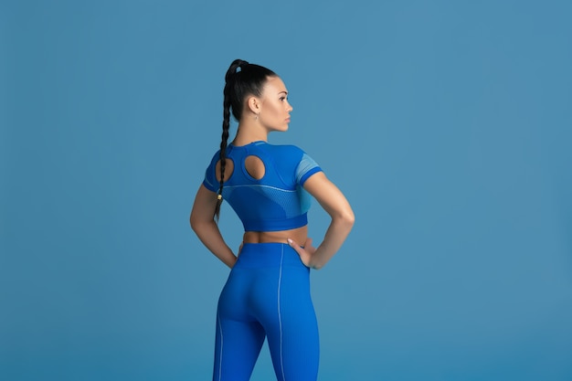Sensual posing. Beautiful young female athlete practicing in studio, monochrome blue portrait