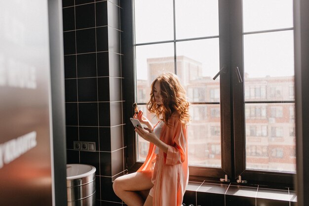 Sensual redhaired girl with makeup brush posing in bathroom Portrait of caucasian cute lady doing skincare routine