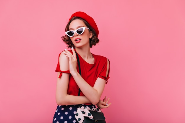 Sensual white lady in french hat posing. Indoor photo of amazing curly girl in red beret enjoying.