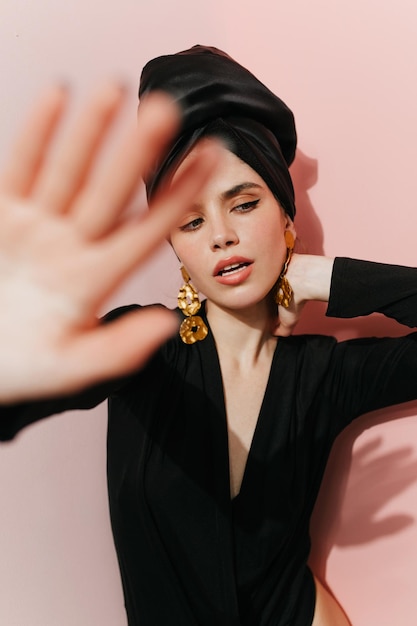 Sensual white woman in turban waving hand Studio shot of european girl in black outfit isolated on pink background