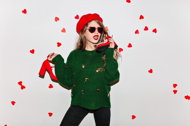 Sensual woman in elegant beret posing with red high heel shoes in hands