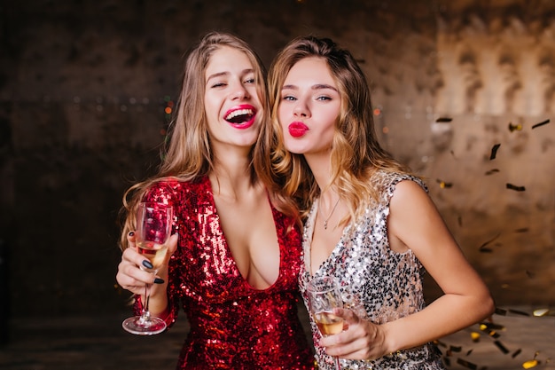 Free photo sensual woman in red trendy dress happy laughing while her female friend posing with kissing face expression