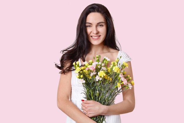 Sensual woman with toothy smile, holds flowers closely