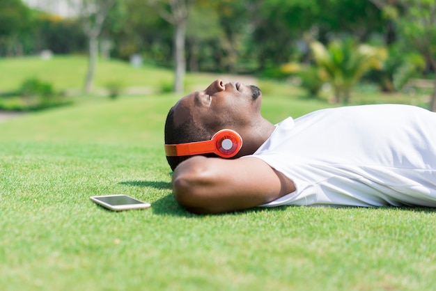 Serene black man resting in park and listening to music. 