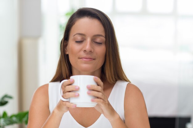 Serene young woman enjoying scent of coffee