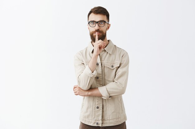 Serious adult bearded man in glasses posing against the white wall
