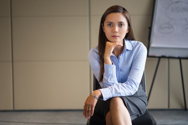 Serious Adult Businesswoman Sitting near Flipchart