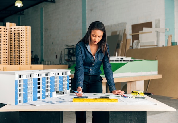 Serious African-American lady with pen standing near model of building on table