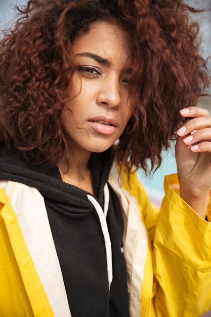 Serious african curly young woman wearing yellow coat