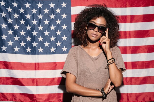 Serious african young lady standing over USA flag