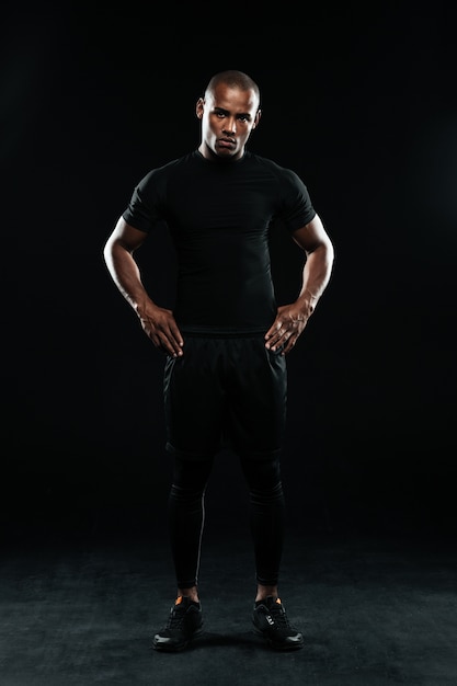Серьезный афроамериканский спортивный человек, стоящий с руками на бедрах