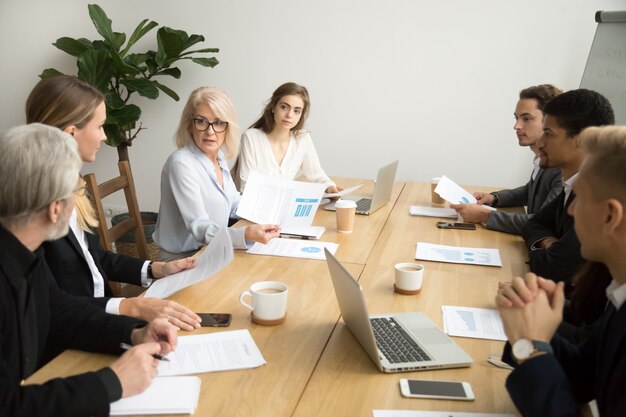 チームミーティングで企業の財務報告書を議論する真剣な年配のビジネスウーマン