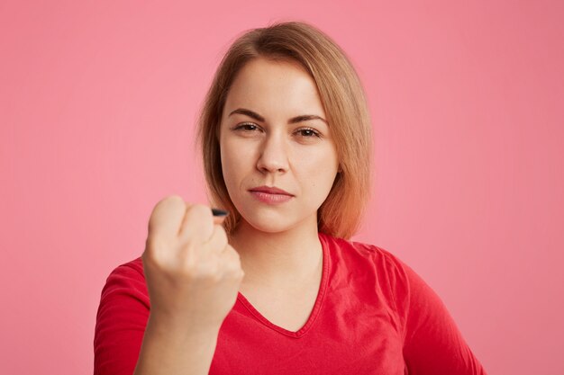 Serious angry woman puts up fist as tries to warn you, dressed in red sweater