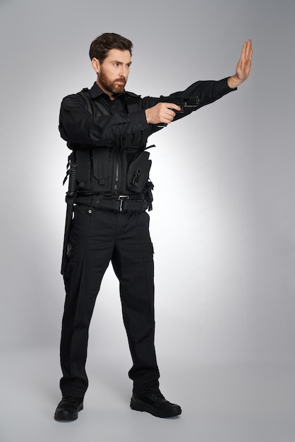 Бесплатное фото Серьезный вооруженный полицейский делает жест остановки с помощью бокового взгляда на человека в полицейской форме