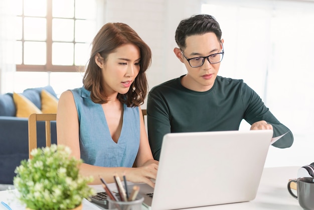 Free photo serious asian husband checking analyzing statement utilities bills sitting together at home.