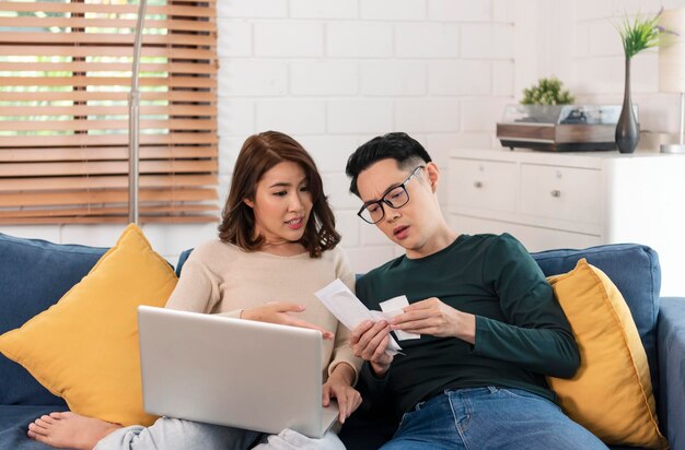 Serious Asian husband checking analyzing statement utilities bills sitting together at home