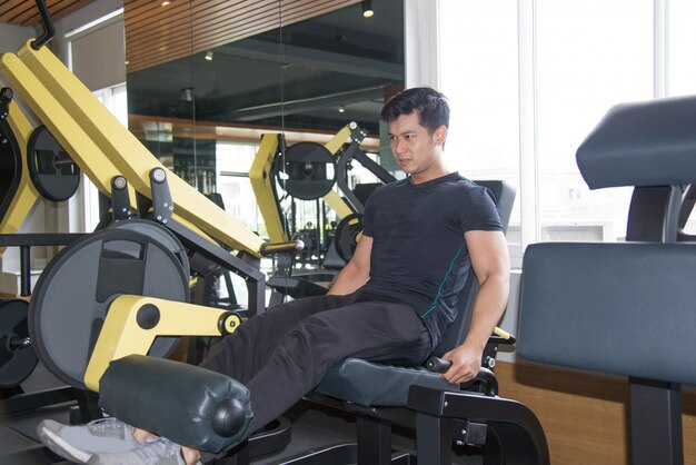 Serious Asian man training legs on exercise machine