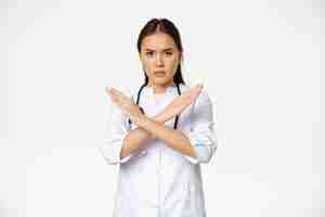Foto gratuita il medico serio della donna asiatica proibisce il comportamento del paziente, mostrando stop, gesto di braccia incrociate, accigliato dispiaciuto, disapprovare smth cattivo, in piedi su sfondo bianco