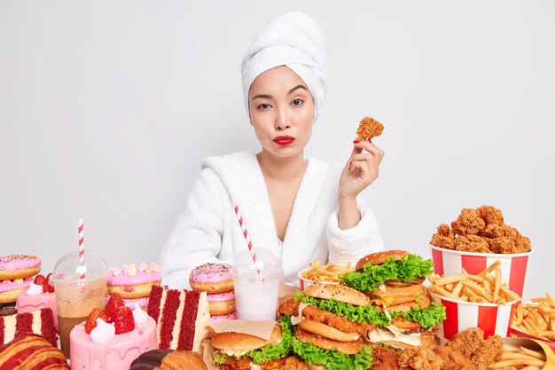 Серьезная азиатская женщина с красными губами, здоровая кожа держит вкусные наггетсы, ест вкусные закуски, пристрастие к фаст-фуду