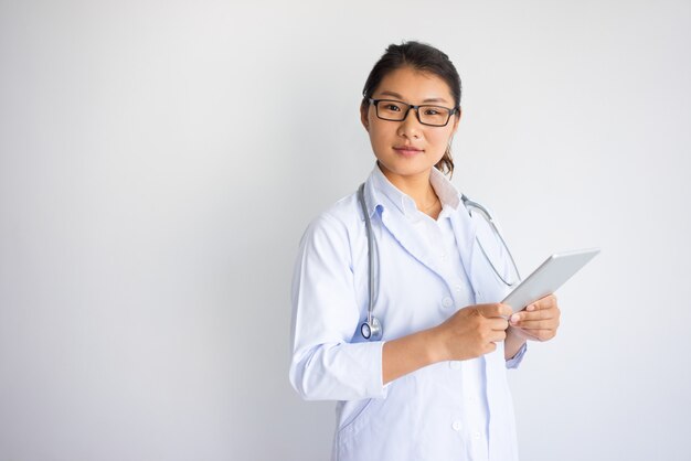 Serious Asian young female doctor using tablet computer.