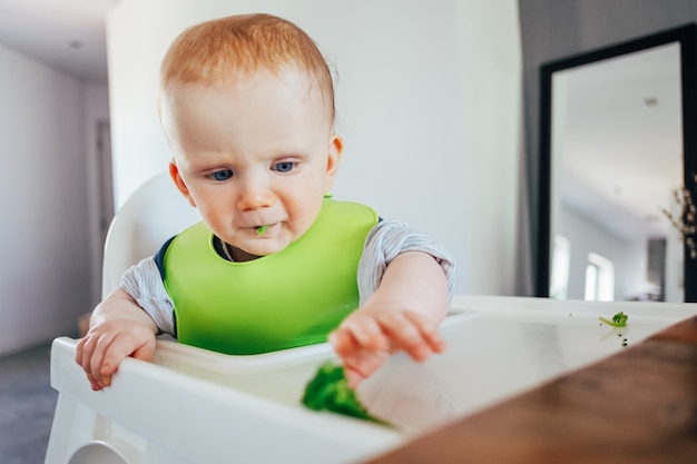 Serious baby girl sitting on highchair and grabbing finger food