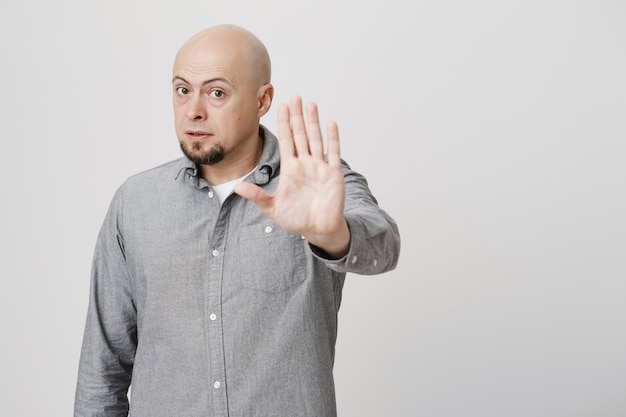 Serious bald man tell to stop, stretch hand disapproval gesture