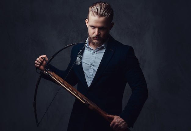 Free photo a serious, bearded male dressed in a suit holds crossbow.