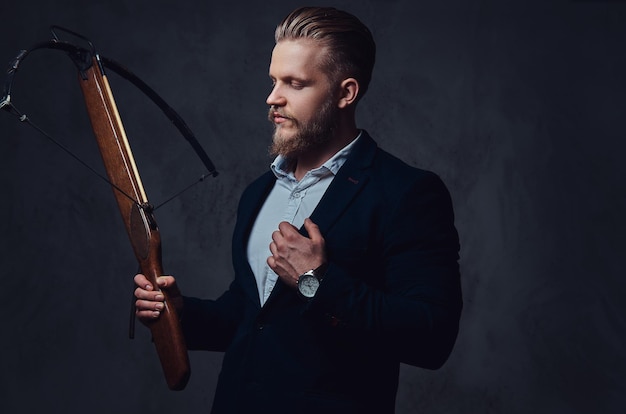 Free photo a serious, bearded male dressed in a suit holds crossbow.