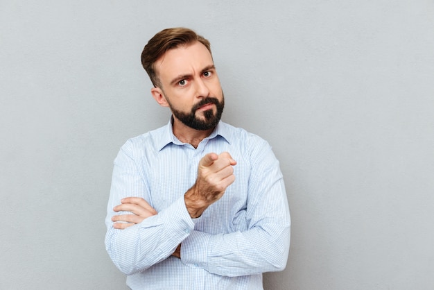 Serious bearded man in business clothes pointing at camera