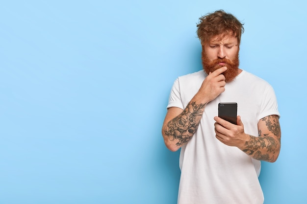 Серьезный бородатый мужчина внимательно смотрит в экран, читает новости в сети, обновляет программное обеспечение