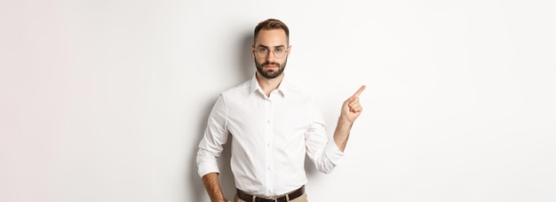 Serious bearded man pointing finger left showing advertisement standing over white background