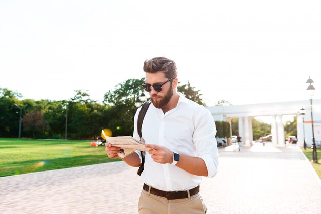 Serious bearded man reading newspaper outdoors