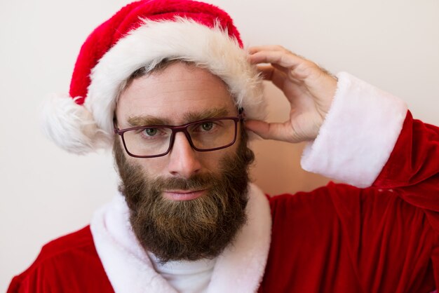 Serious bearded man wearing Santa Claus costume and glasses