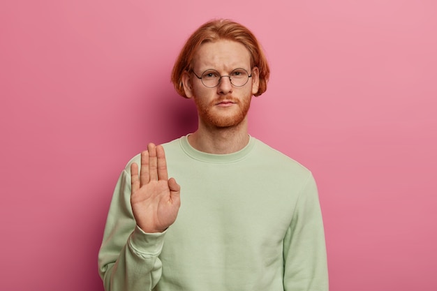 Serious bearded redhead man shows palm in stop gesture