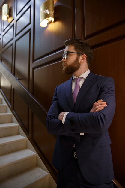 Serious bearded young businessman standing with arms crossed