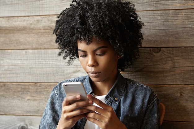 携帯電話でインターネットを閲覧しながらニュースを読んでいる深刻な美しいアフリカ系アメリカ人の女の子