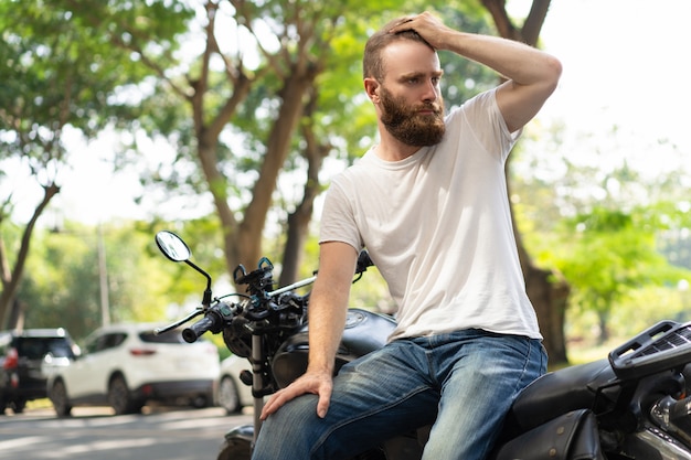 Serious biker leaning on broken motorbike